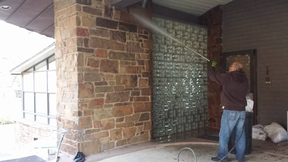 A Metroplex technician pressure washing a stone and glass-block entry