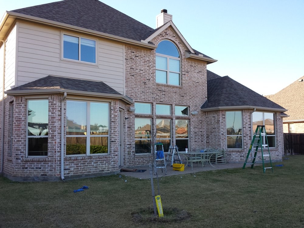 Back of a brick home with sparkling clean tall windows and ladders on the patio