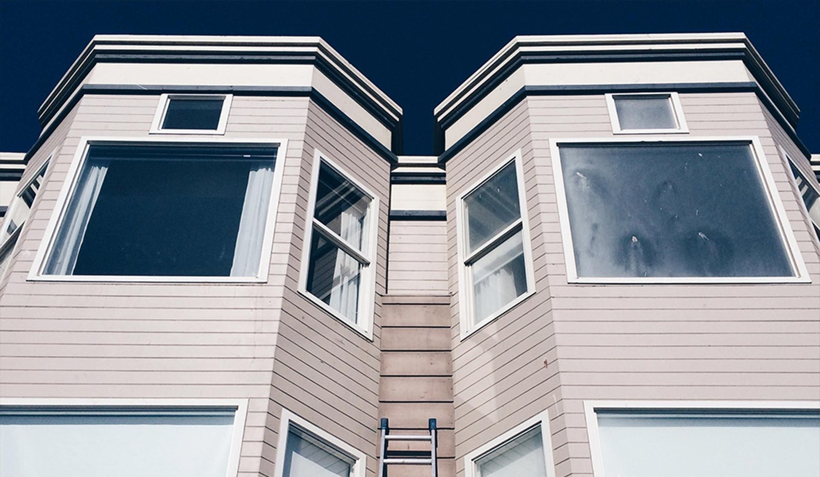 Tall clean windows on the front of a light-colored home, seen from below