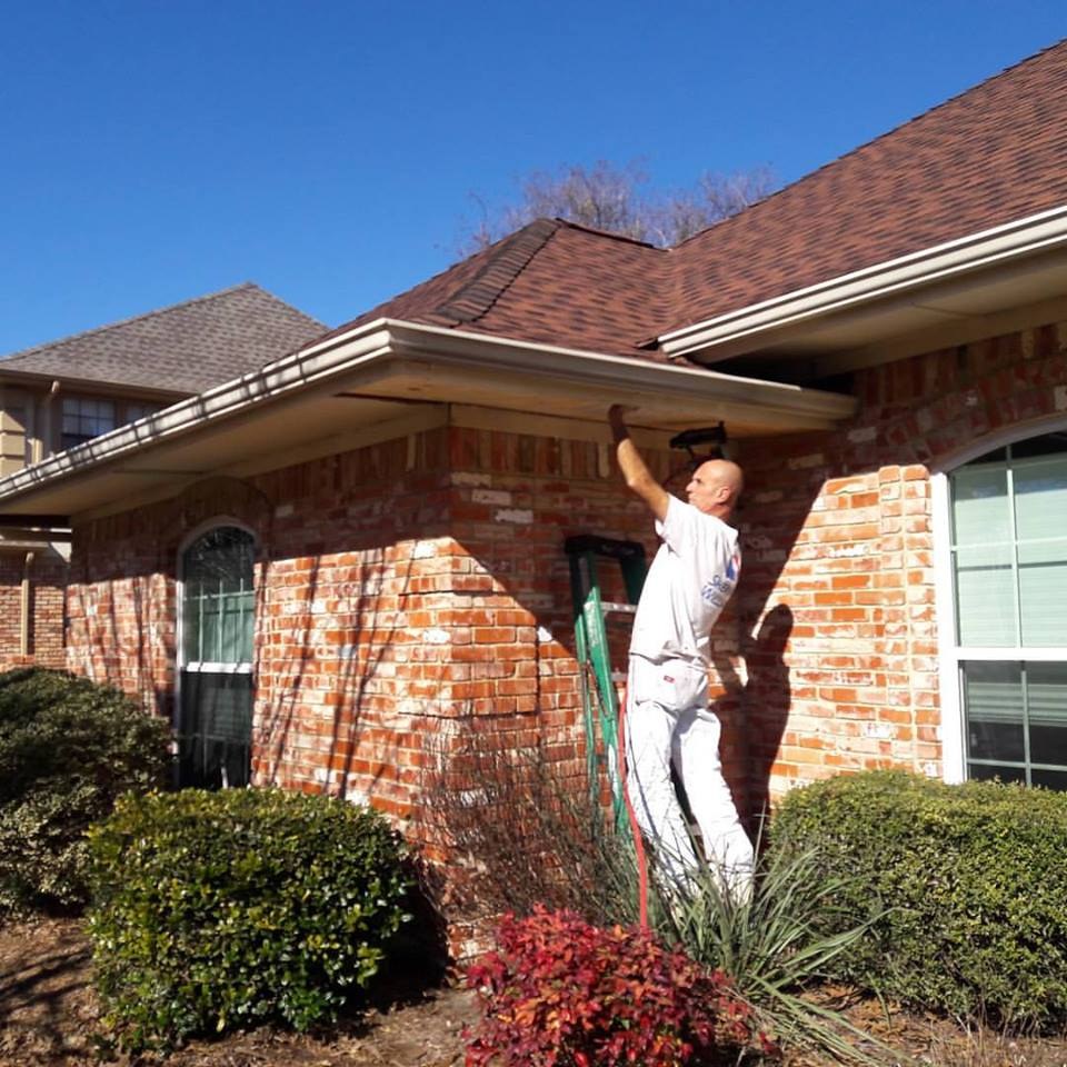 A Metroplex worker on a ladder at the gutter of a brick home