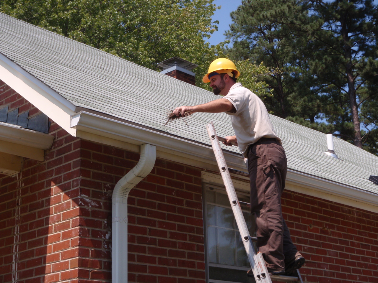 A technician on a ladder cleaning the gutter of a brick home