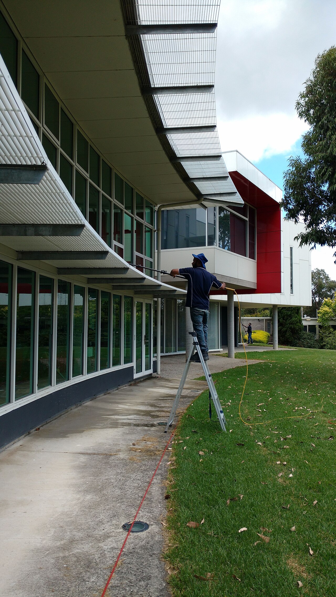 A technician cleaning the windows of a glass-fronted building with a water-fed pole